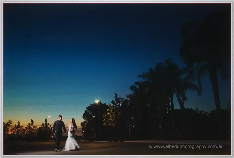 Bride and groom stroll beneath palm silhouettes against a deep blue twilight sky at Caversham House