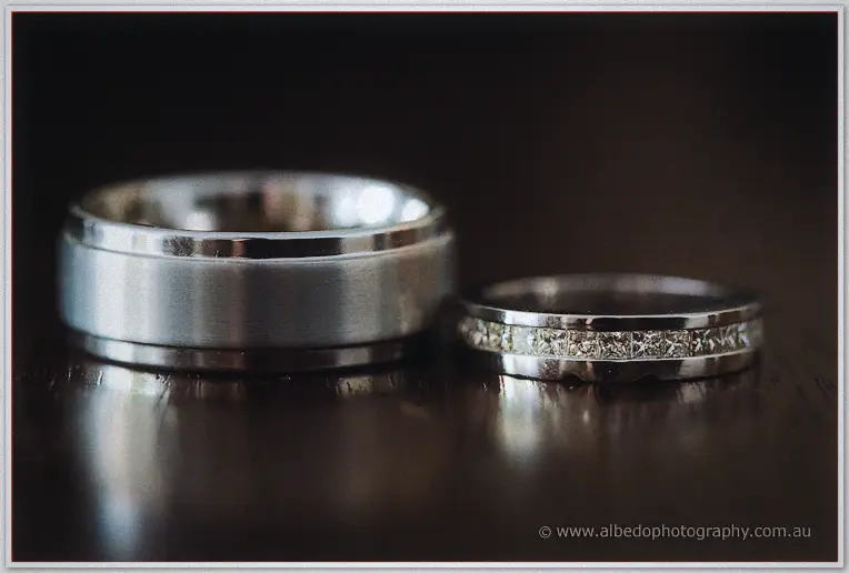 The bride's diamond band and the groom's polished ring resting side by side on dark timber