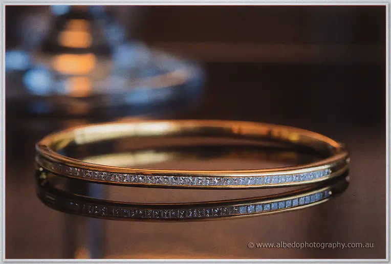 A gold diamond-set bangle catches the light on a dark reflective table