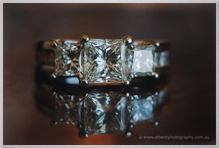 Close-up of Haley's three-stone princess-cut engagement ring sparkling on dark timber