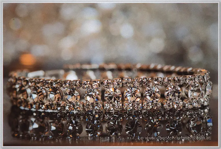 A crystal-studded bridal bracelet glints on a mirror amid glittering bokeh in the wedding morning light