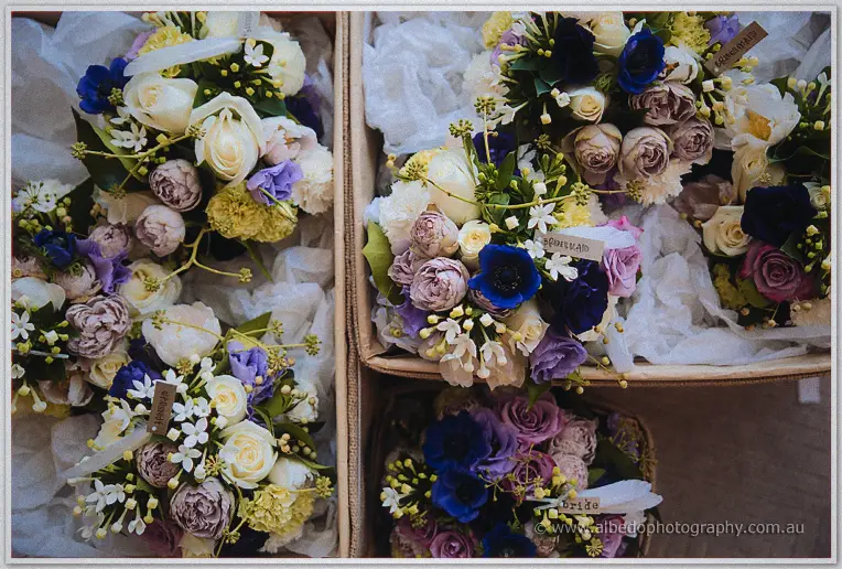 Bridesmaid bouquets of mauve roses, blue anemones and cream blooms wait in labelled boxes