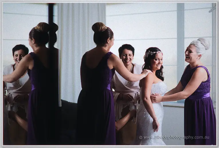 Haley's bridesmaids in purple gowns laugh while helping her into the dress before Caversham House celebrations