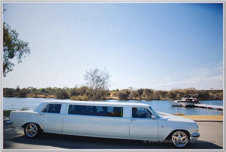 White stretch limousine parked beside the Swan River under a clear blue sky as the party arrives