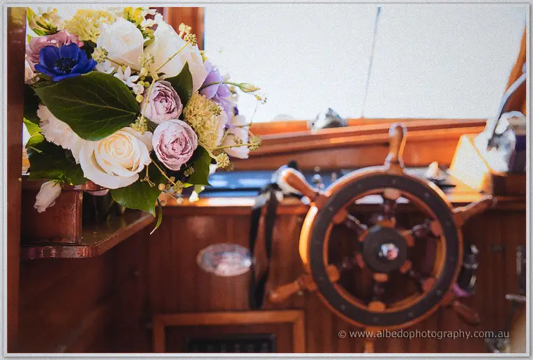 Haley's white and lavender bouquet rests by the polished wooden wheel inside the vintage cruiser's cabin