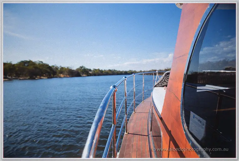 Chrome rail and polished deck of the vintage cruiser gliding along the tree-lined Swan River in sunshine