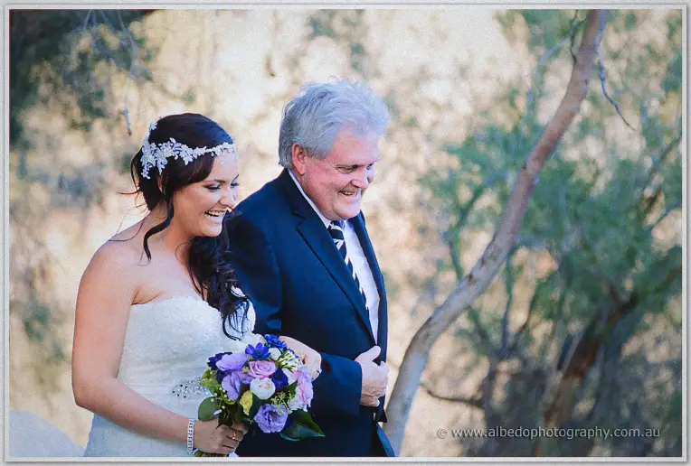 Haley laughs beside her father as he walks her toward the garden ceremony in golden afternoon light