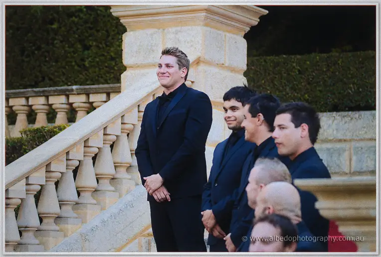 Groom Matt smiles from the limestone balustrade as his groomsmen gather behind him at Caversham House