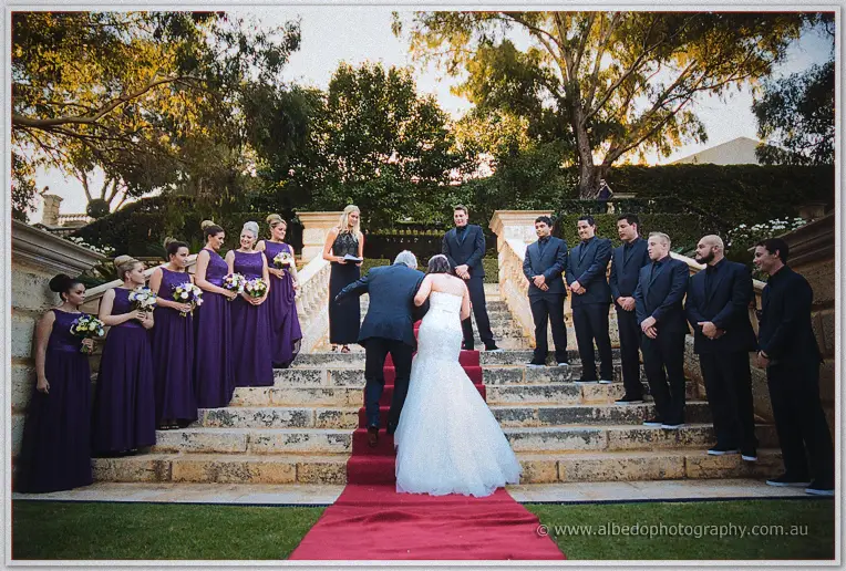 Haley reaches the red-carpeted steps where Matt, bridesmaids and groomsmen await beneath golden gums