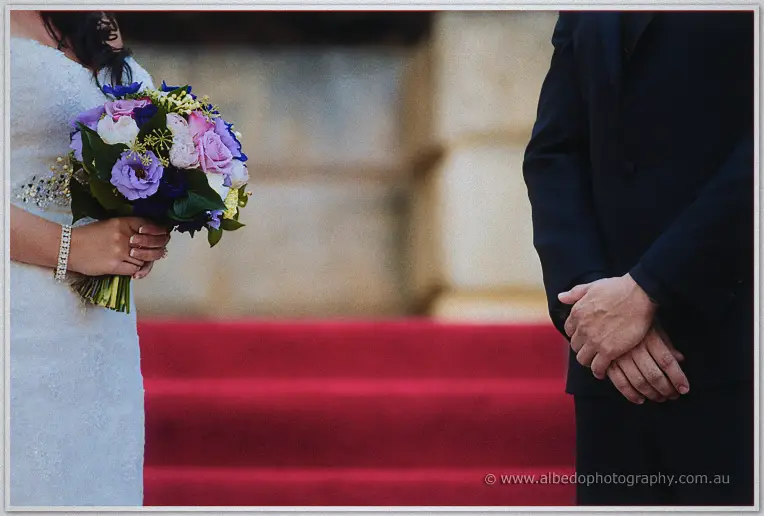 Haley holds her purple bouquet before Matt's clasped hands on the sunlit ceremony steps