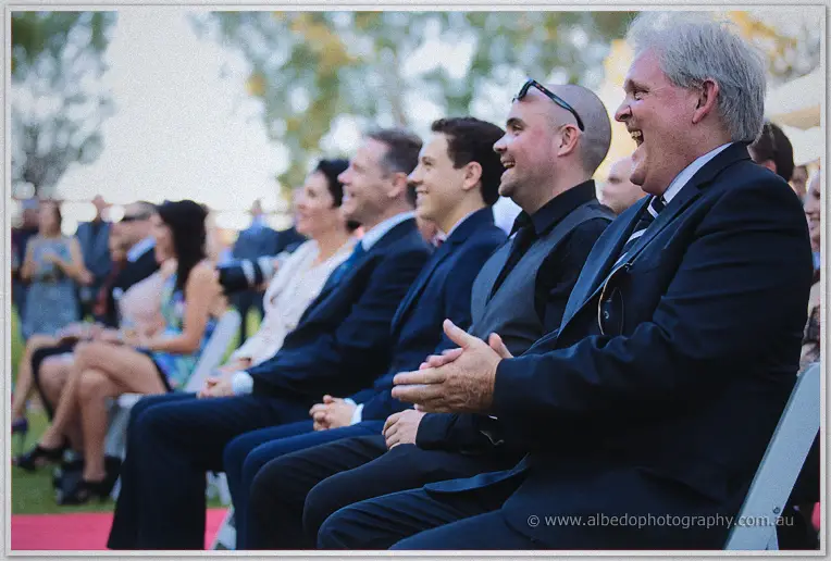Haley's father laughs while clapping among the seated guests at the garden ceremony
