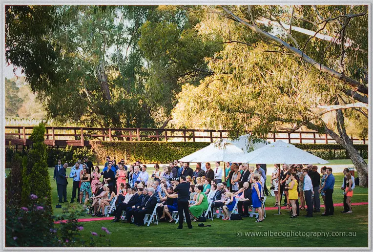 Guests under white umbrellas watch the Caversham lawn ceremony framed by towering sunlit gums