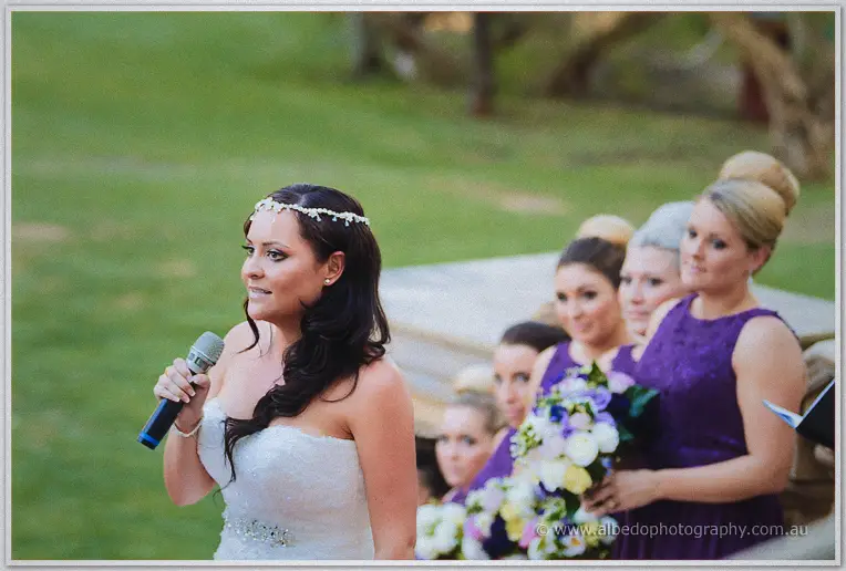 Haley speaks earnestly into the microphone as her bridesmaids watch from behind in purple