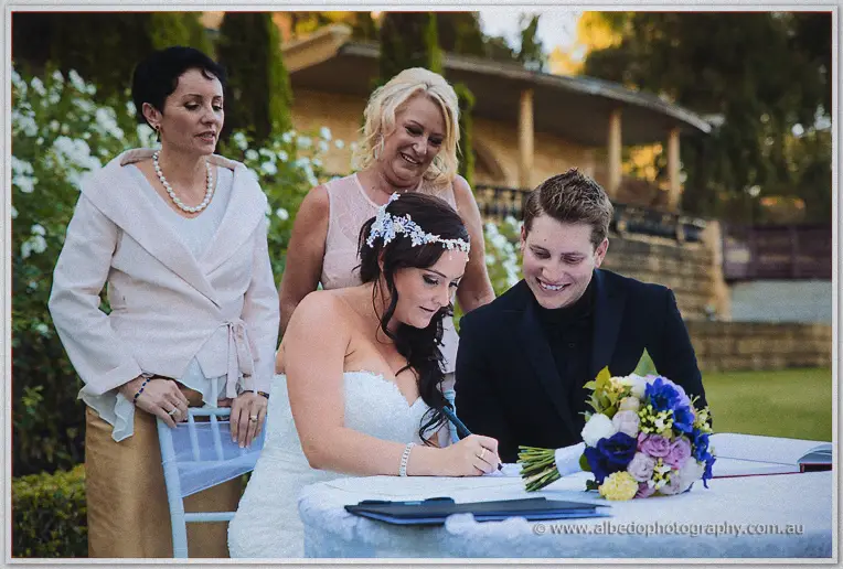Haley signs the marriage register beside Matt as their mothers watch among white garden roses