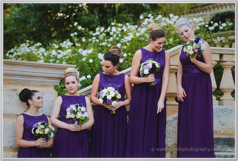 Five bridesmaids in floor-length purple lace gowns hold white bouquets on Caversham House's stone steps.