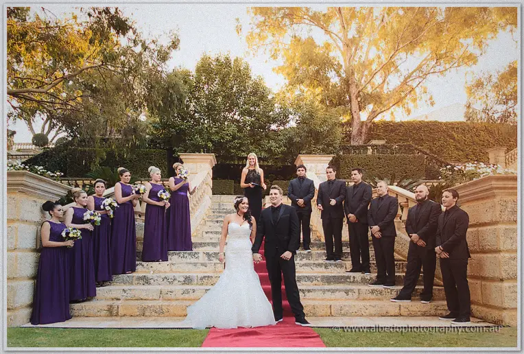 The bridal party lines a grand limestone staircase as Haley and Matt stand hand in hand below at golden hour.