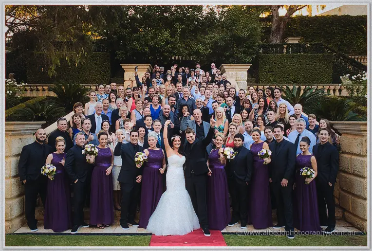 A jubilant crowd of guests fills the terraced steps behind Haley and Matt, arms raised in celebration.