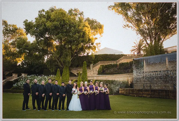 The bridal party gathers on the lawn beneath Caversham House's gardens and waterfall at sunset.