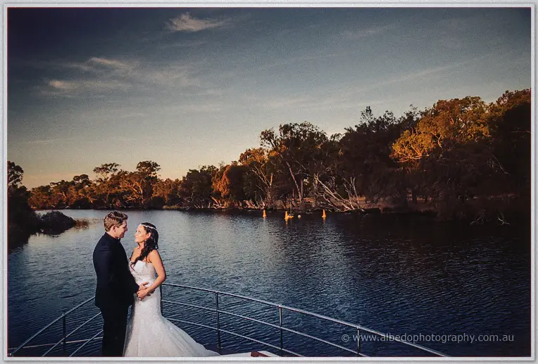 Haley and Matt gaze at each other on the boat's bow, dusk settling over the calm river and golden treeline.