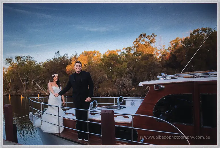 Haley and Matt walk the deck of the timber river launch hand in hand beneath a clearing evening sky.