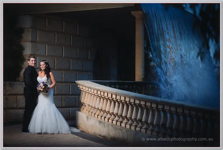 Haley and Matt pose by the stone balustrade as water cascades down the illuminated waterfall wall at night.