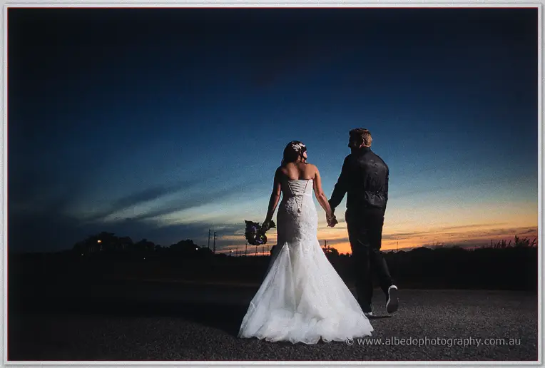 Haley and Matt walk the road hand in hand, her lace train sweeping the bitumen under a fiery sunset.
