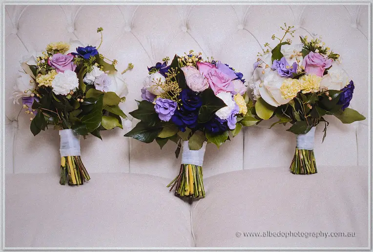 Three pastel bouquets of roses, carnations and sweet peas lean against a cream buttoned headboard