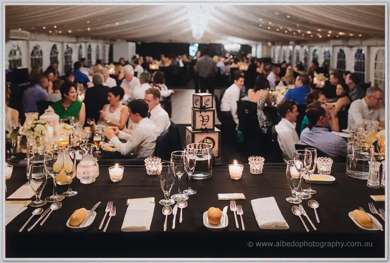 Guests dine beneath the draped marquee at candlelit tables dressed with black linen and glassware.