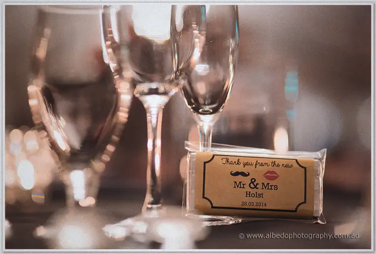 A wrapped chocolate bar favour reading 'Thank you from the new Mr & Mrs Holst' leans against champagne flutes.