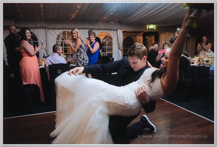 Matt dips Haley low on the dance floor, her bouquet arm high as guests cheer and film around them.