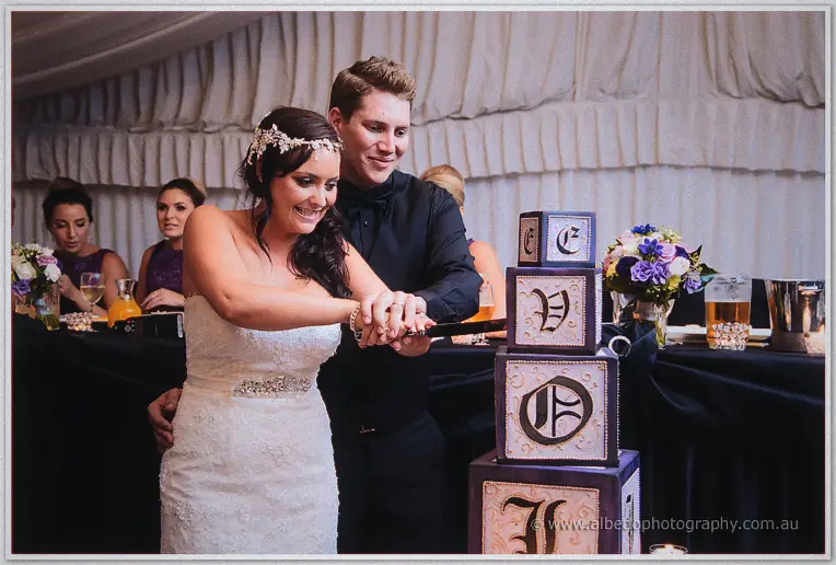 Haley and Matt cutting their lettered box cake, smiling, at the Caversham House bridal table