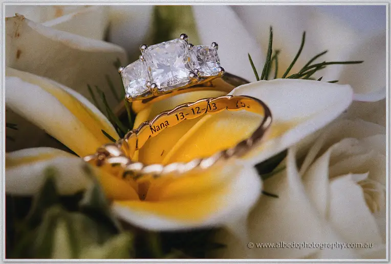 Three-stone diamond ring and gold band engraved Nana 13-12-13 nestled in a frangipani bloom