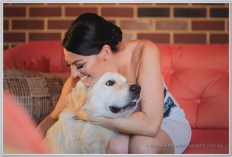 Stacey kneeling on a coral couch hugging her golden retriever against an exposed brick wall