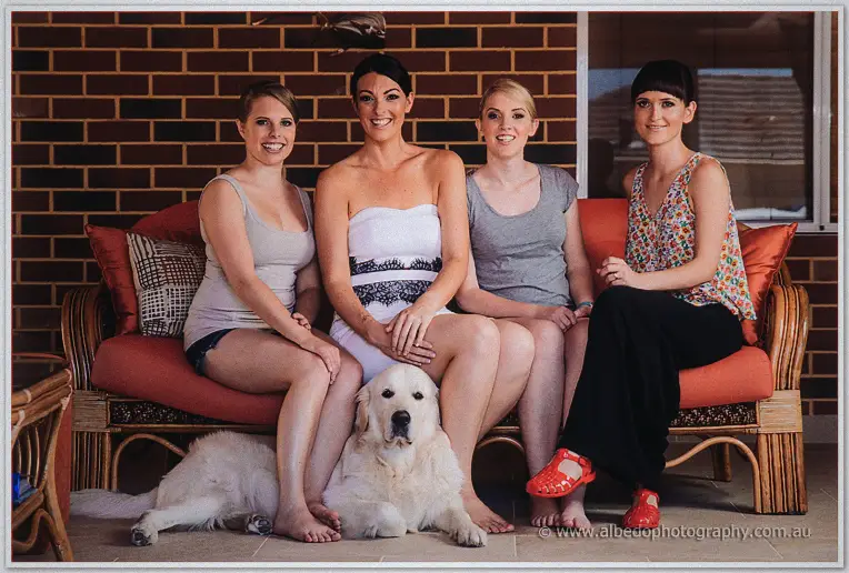 Stacey with her three bridesmaids on a cane couch, two golden retrievers lounging at their feet