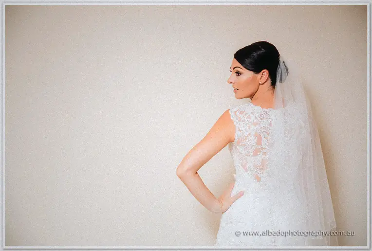 Stacey glancing back over her shoulder, veil trailing down the illusion lace back of her gown