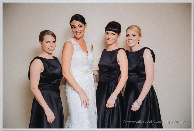 Stacey standing with her four bridesmaids in matching black satin dresses against a plain wall
