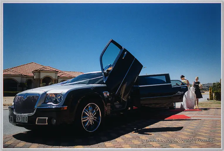 Bridesmaids stepping from a black stretch limousine onto a red carpet under a blazing blue sky