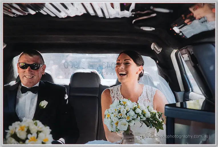 Stacey laughing beside her tuxedoed father in sunglasses as the limousine carries them off