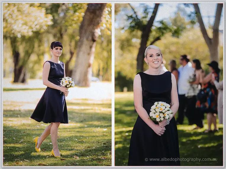 Bridesmaids in navy dresses with yellow heels carry white and yellow bouquets on the lawn.