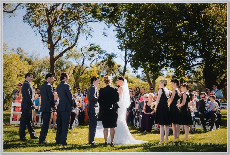 The celebrant joins Stacey and Nathain before guests beneath the shaded riverside trees.