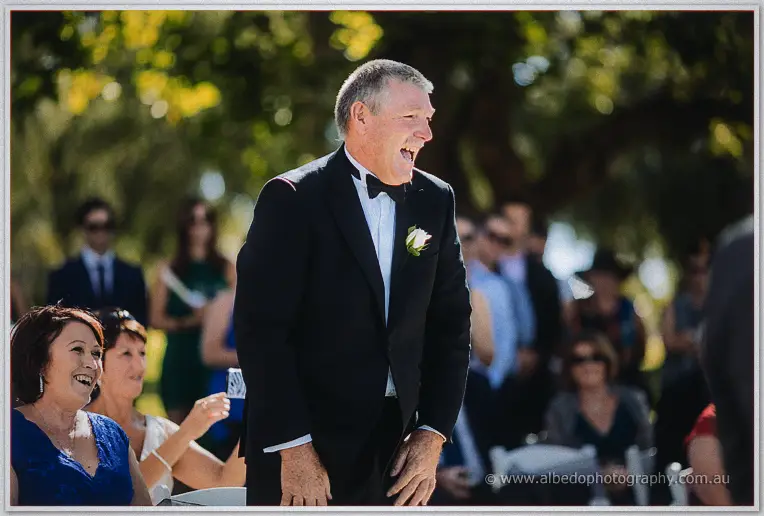 Stacey's father laughs heartily in his black bow tie among seated wedding guests.