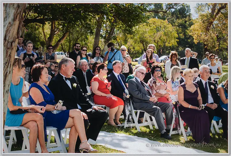 Rows of guests in colourful attire watch the ceremony from white folding chairs.