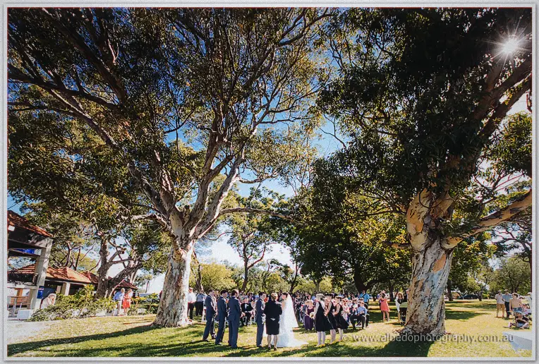 A wide view shows the bridal party and guests gathered between huge eucalypts at Matilda Bay.