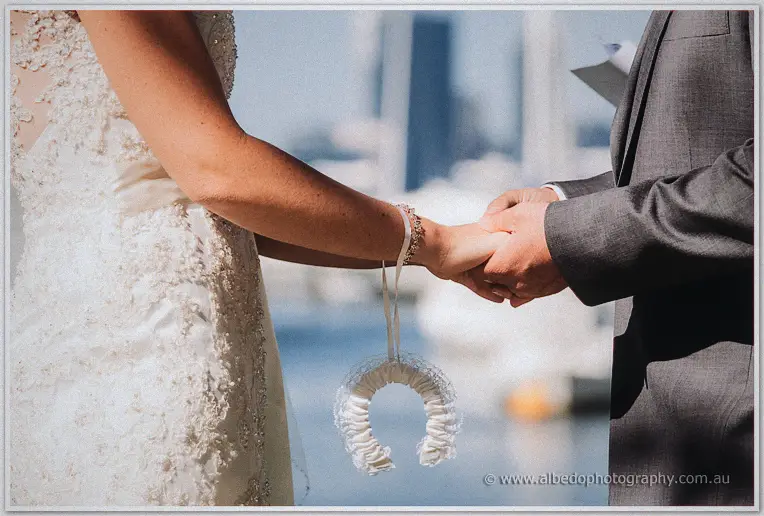Nathain takes Stacey's hand, a ribboned horseshoe dangling from her wrist, boats blurred behind.