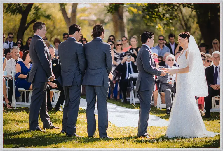 Nathain slides the ring onto Stacey's finger as guests watch from the garden aisle.