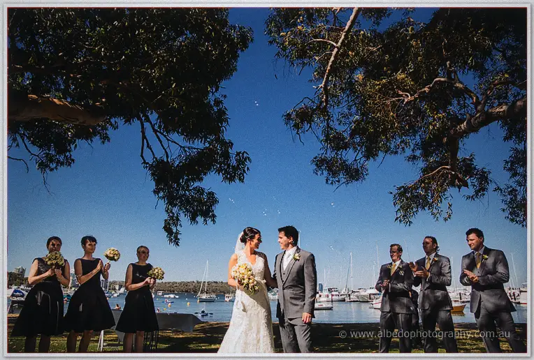 Stacey and Nathain grin at each other as their bridal party applauds by the moored yachts.