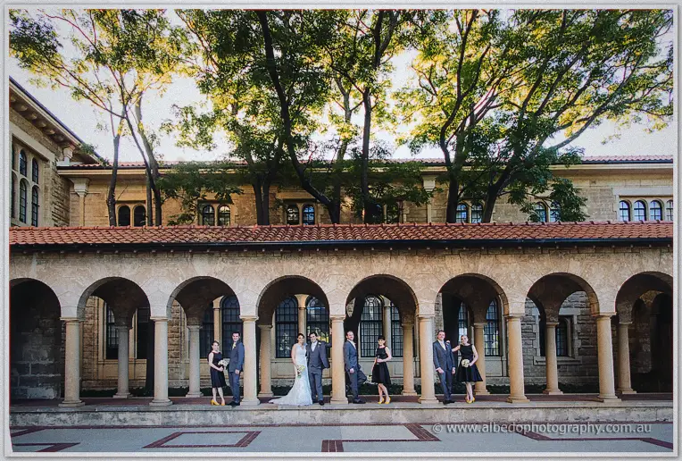 A wide view of the wedding party lined up beneath a long arcade of stone arches.