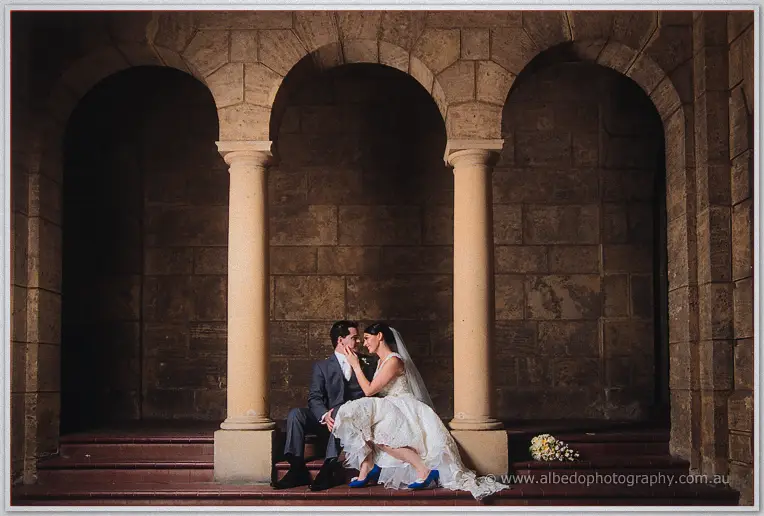 Stacey cradles Nathain's face on the shadowed stone steps, her blue heels bright beside them.