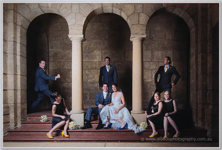 The playful bridal party strikes poses across the dim colonnade steps, yellow shoes aglow.