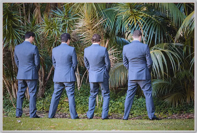 Four groomsmen in slate suits face the palms in a cheeky line on the lawn.